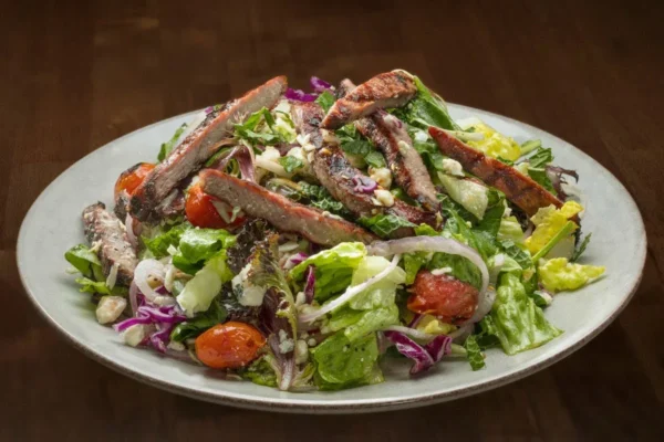 Fresh salad topped with grilled steak slices, tomatoes, and greens at Wood Ranch BBQ & Grill in Agoura Hills