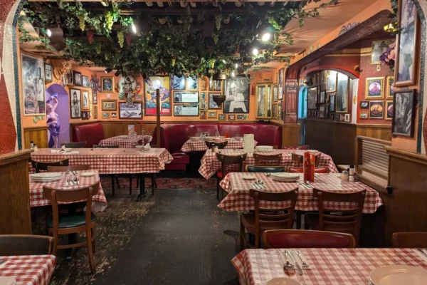 Colorful Buca di Beppo dining room with red booths, checkered tables, and vine-covered ceiling.