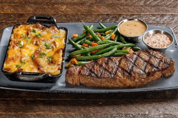 Grilled steak with cheesy potato gratin and green beans on black plate