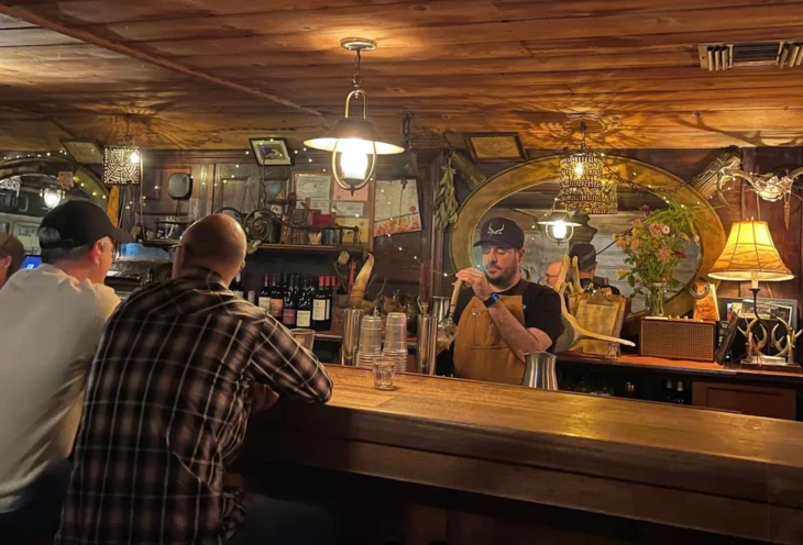 the_old_place_bar_evening Bartender preparing drinks at The Old Place bar with dim lighting, rustic decor, and customers seated nearby.