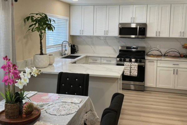 Bright kitchen at Anita’s Care Villa with white cabinets, quartz counters, stainless stove, and a dining table with flowers.