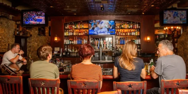 Guests seated at the bar inside Bandits Grill & Bar, watching a live sports game on multiple TV screens in a warm, rustic setting.