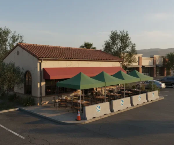 The outdoor dining area at Cronies Sports Grill, featuring tables shaded by green canopy tents and protected by concrete barriers in the parking lot area.
