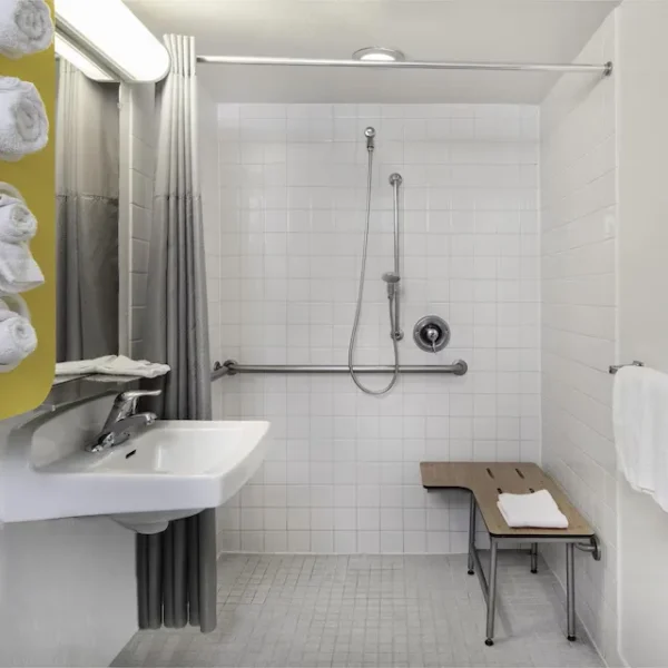 ADA accessible bathroom with roll-in shower, grab bars, shower bench, and handheld showerhead.