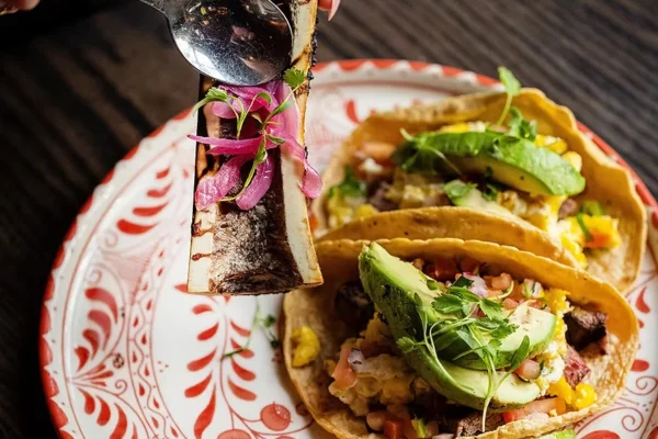 Bone marrow taco topped with pickled onions and herbs, served at RED O restaurant with authentic Mexican presentation.