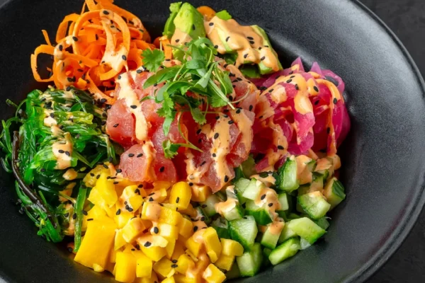 Colorful tuna poke bowl with mango, avocado, seaweed salad, and sesame dressing, served at RED O restaurant.